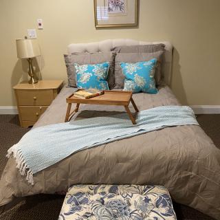 A cozy bedroom setup featuring a neatly made bed with patterned pillows and a decorative throw, complemented by a wooden tray on the bed.
