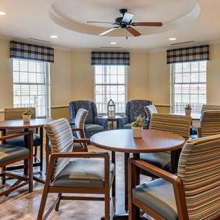 A cozy seating area with tables and chairs, featuring large windows and a ceiling fan.