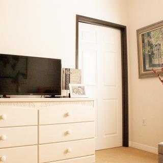 A cozy bedroom corner featuring a white dresser with a TV on top, adjacent to a door and a framed mirror on the wall.