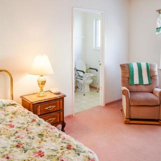 A cozy bedroom with floral bedding, a nightstand with a lamp, and an armchair.