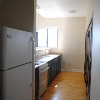 A narrow galley kitchen with appliances and wood flooring.