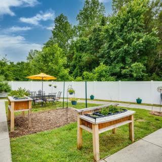 A backyard garden with raised beds, patio furniture, and a white privacy fence.