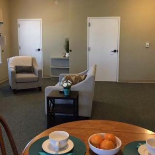 A minimalistic living room with cozy chairs and a small table set with fruit and tea cups.
