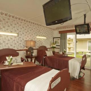 A hospital room with two patient beds and a wall-mounted television.