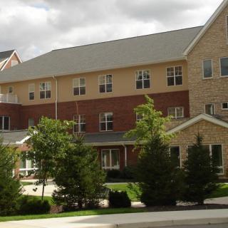 A multi-story residential building with a brick exterior and surrounded by trees under a cloudy sky.