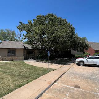 A peaceful residential scene showcasing a house with a large tree and parking space under a clear blue sky.