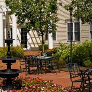 A serene outdoor patio with tables, chairs, and a fountain surrounded by lush greenery and flowers.