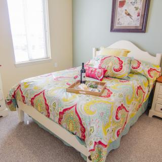 A cozy bedroom featuring a bed with colorful bedding, a window allowing natural light, and decorative elements like a wall picture.