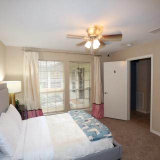 A cozy bedroom with a large window, ceiling fan, and a neatly made bed.