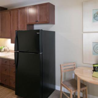 A modern kitchen with a black refrigerator, wooden cabinets, and a small dining table with chairs.