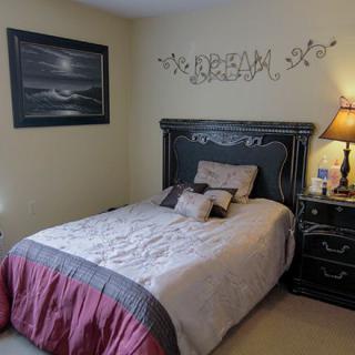 A cozy bedroom with a neatly made bed, wall artwork, and a bedside lamp.