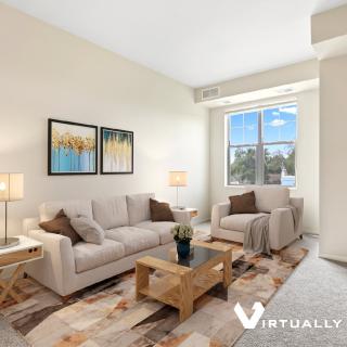 A cozy living room with a comfortable sofa set, wooden coffee table, wall artwork, and a large window allowing natural light to fill the space.