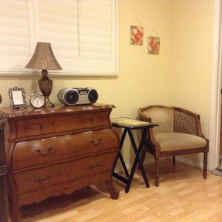 A cozy corner featuring a vintage wooden dresser adorned with decorative items, a lamp, and a comfortable chair.