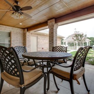 A cozy outdoor patio with a table and chairs under a covered area featuring a ceiling fan.