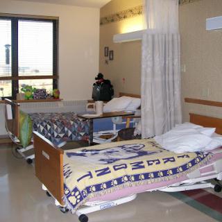 A view of a patient room in a hospital, featuring two beds and a window.