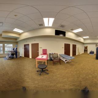 A panoramic view of a medical or hospital room, featuring office furniture and a patient bed.