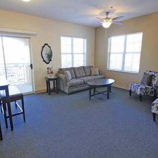 A cozy living room with a sofa, chairs, and tables under natural light from large windows.