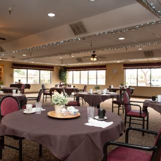 A well-decorated dining room with neatly arranged tables and chairs, featuring elegant lighting and window views.