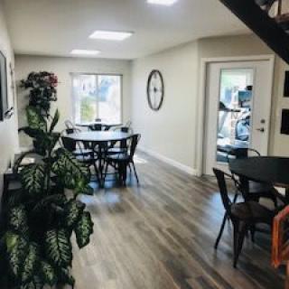A cozy indoor dining area with multiple tables and chairs, decorated with plants and a wall clock.