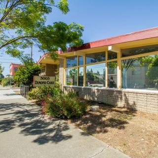 The exterior of a restaurant on a sunny day, featuring trees and a sidewalk.