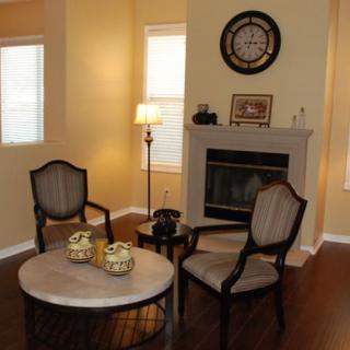 A cozy living room with two chairs, a round coffee table, and a fireplace adorned with a clock.