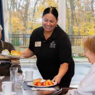 A smiling server delivering meals to elderly diners at a restaurant.