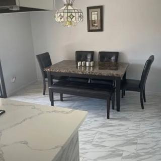 A modern dining room with a marble floor, featuring a dark wooden dining table, chairs, and bench seating under a stylish chandelier.