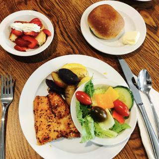A breakfast spread including toast, salad with fresh vegetables, fruit bowl, and bread roll.