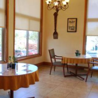 A cozy dining area with round tables and chairs, featuring large windows and a chandelier.