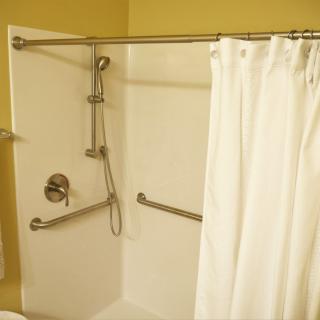 A bathroom with an accessible shower featuring grab bars and a handheld showerhead, enclosed by a white curtain.