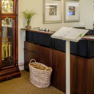 A reception area featuring a desk, grandfather clock, decorative plant, and wall art.