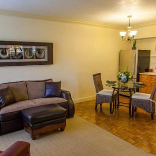 A cozy living room with a sofa, dining table, and chandelier, featuring wooden flooring and stylish decor.