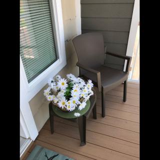 A cozy patio setup with a chair and a small table adorned with a daisy flower arrangement.