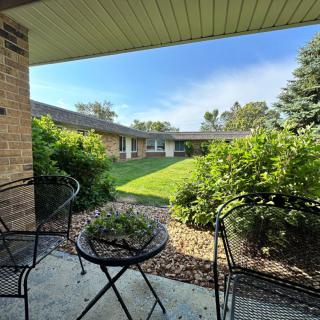 A cozy patio with outdoor seating overlooks a lush garden and well-maintained lawn on a sunny day.