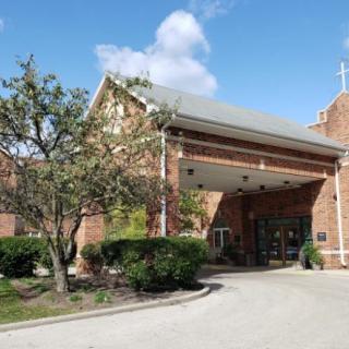 A brick church entrance with surrounding landscaping and a clear sky.
