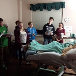 A group of young individuals visiting a patient in a hospital room.