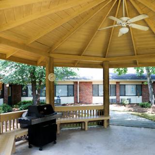 A spacious gazebo featuring a grill and ample seating, surrounded by greenery.