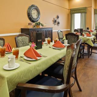 A well-set dining room with tables prepared for guests, featuring green tablecloths and red napkins.
