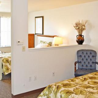 A well-lit hotel room featuring a cozy bed, a decorative vase on a shelf, and an upholstered chair.