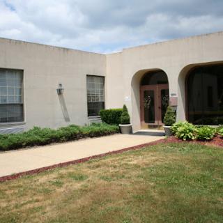 A modern building with a welcoming entrance, surrounded by well-maintained landscaping under a cloudy sky.