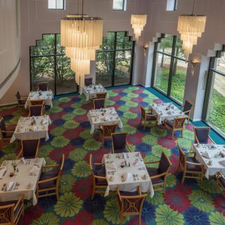 A well-lit restaurant interior with elegantly set tables and colorful carpet.