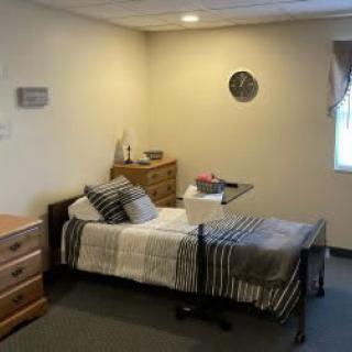 A cozy bedroom with a bed, dressers, and a wall clock.