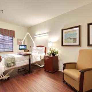 A comfortable hospital room featuring a bed, a chair, and warm lighting, designed for patient care.