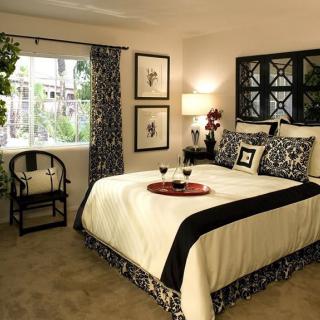 A stylish and cozy bedroom with elegant decor, featuring a neatly made bed with patterned bedding, a bedside lamp, and an armchair by the window.