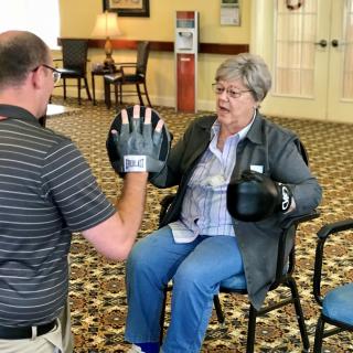 An elderly woman participates in a boxing exercise session with a trainer.