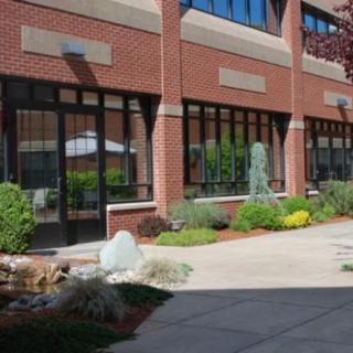 A brick building with large windows, surrounded by landscaped shrubs and a pathway.