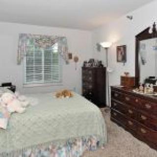A cozy bedroom featuring a bed with a quilt, a dresser with a mirror, and various decorative elements.