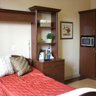A cozy bedroom with a bed, bookshelf, and microwave.