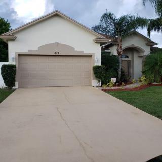 A suburban house with a driveway and garage surrounded by palm trees and a well-maintained lawn.