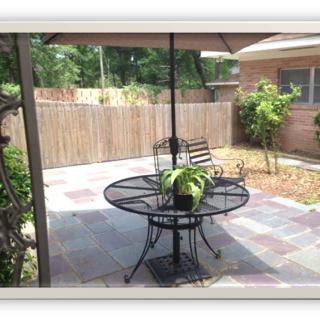 A backyard patio with a round table, chairs, and an umbrella, surrounded by plants.